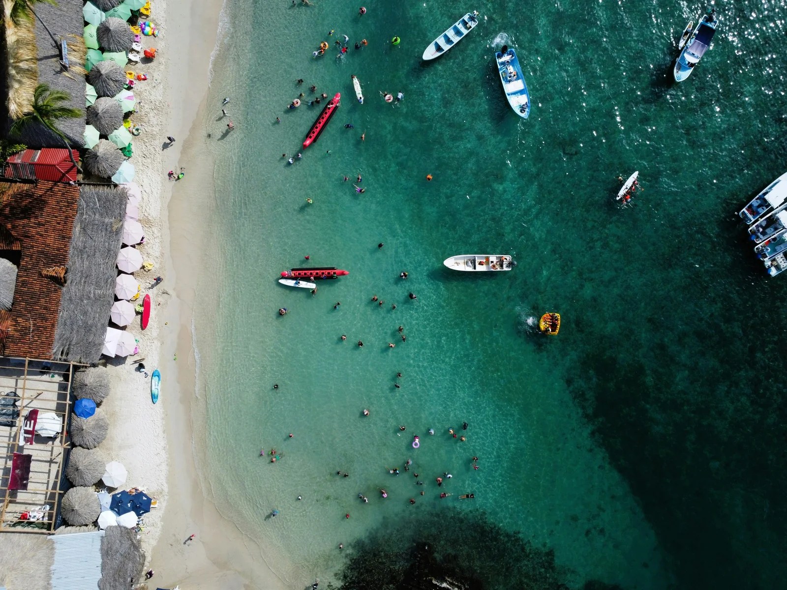 Vista aérea de lanchas y kayaks frente a una playa con palapas
