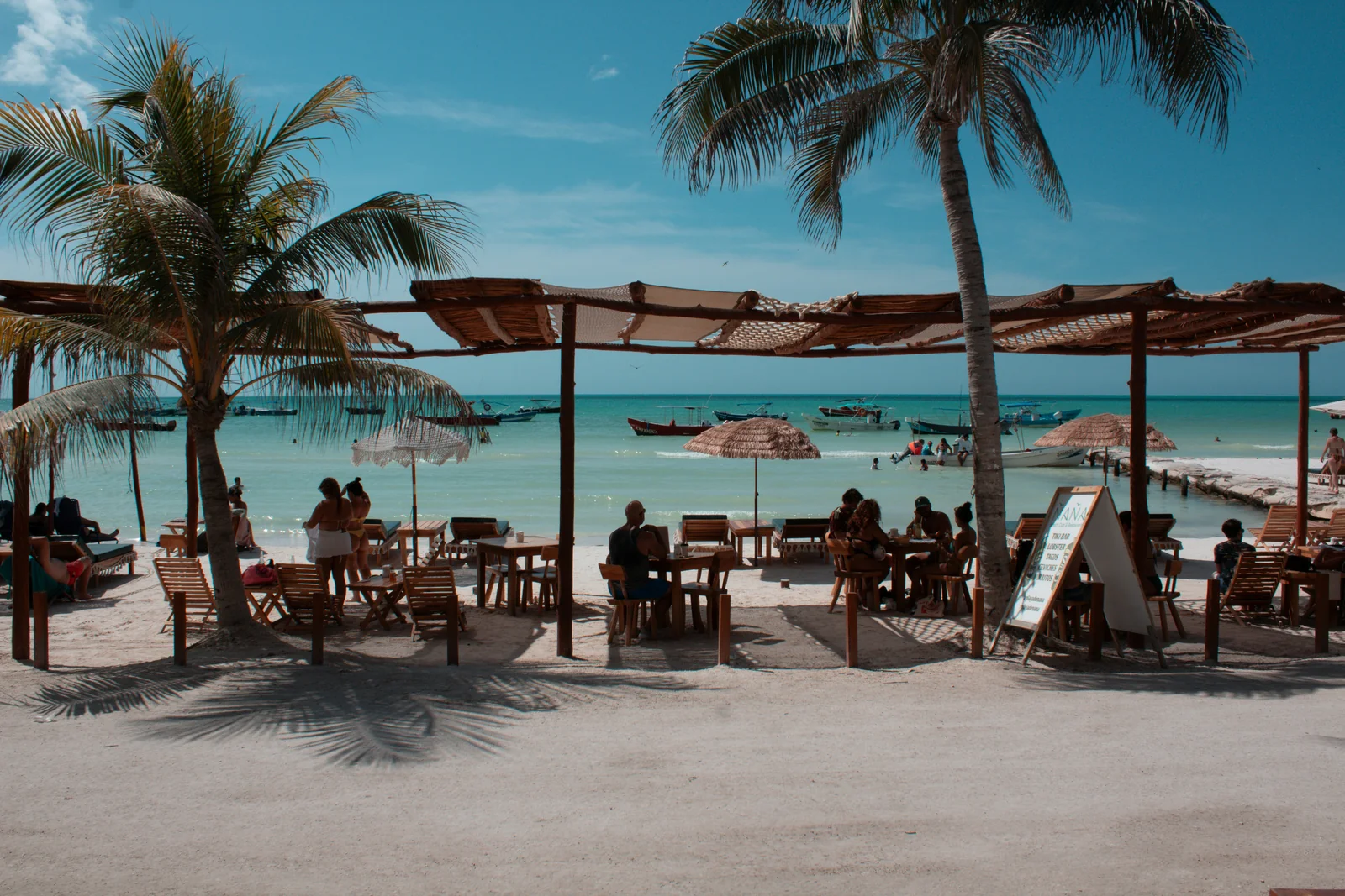 Mesas de un restaurante junto a la playa, entre palmeras y frente al mar